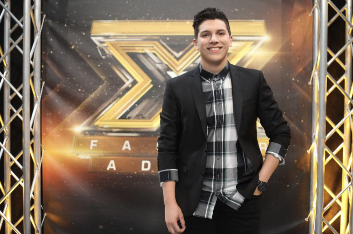 Young ILIJA posing on the X Factor Adria stage in a black blazer and plaid shirt