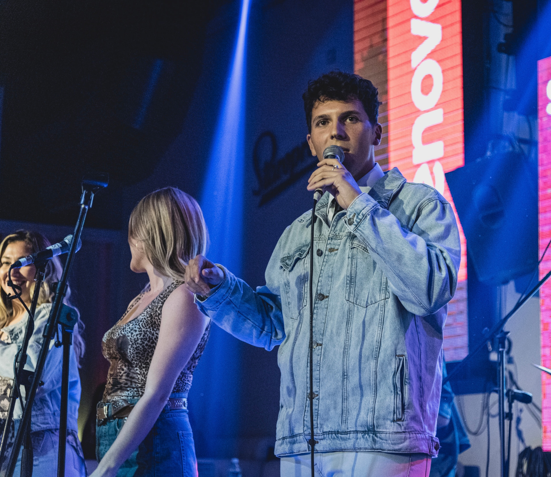 ILIJA in a denim jacket singing on a blue-lit stage with his band