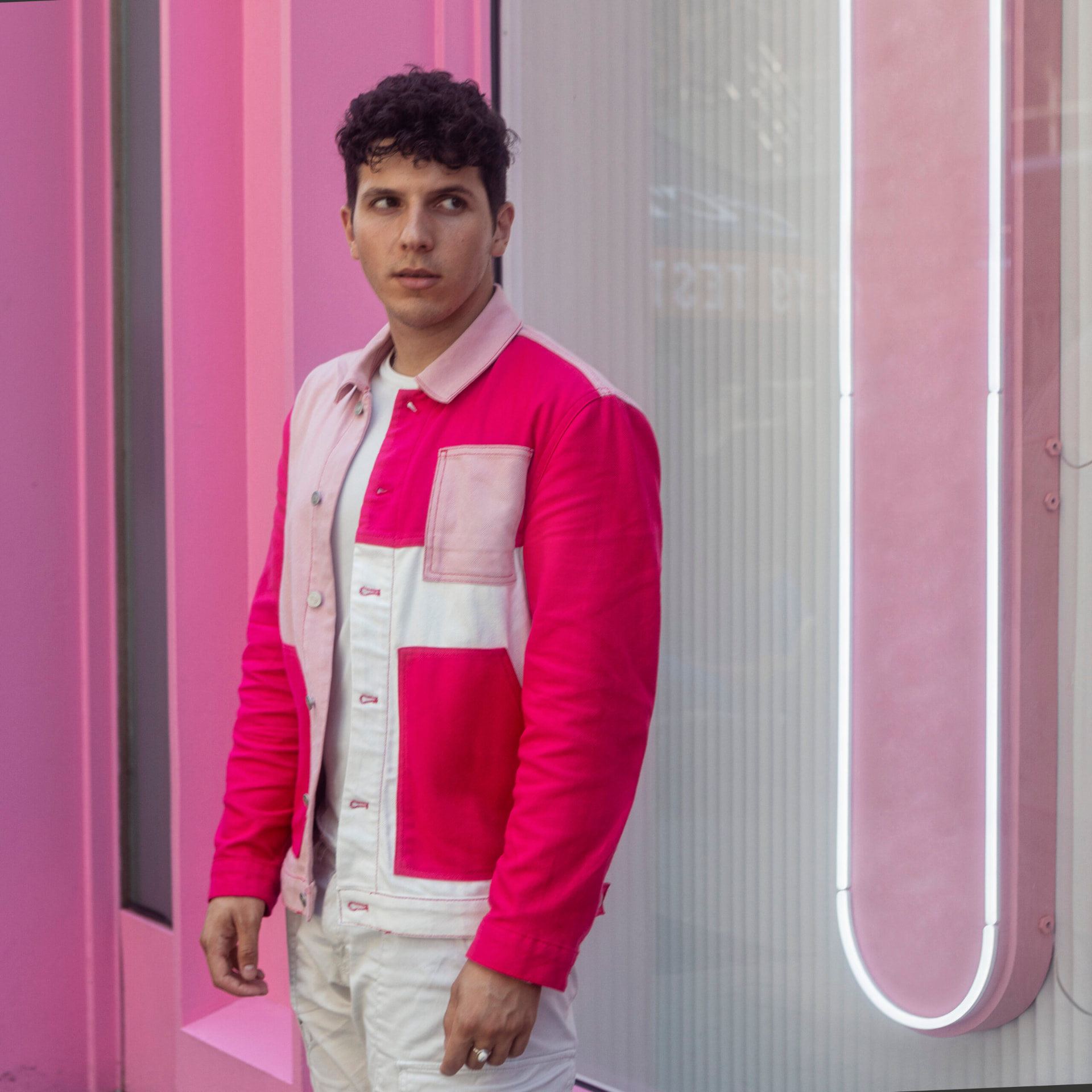 ILIJA in a pink colour-block denim jacket against a bright pink neon-lit wall