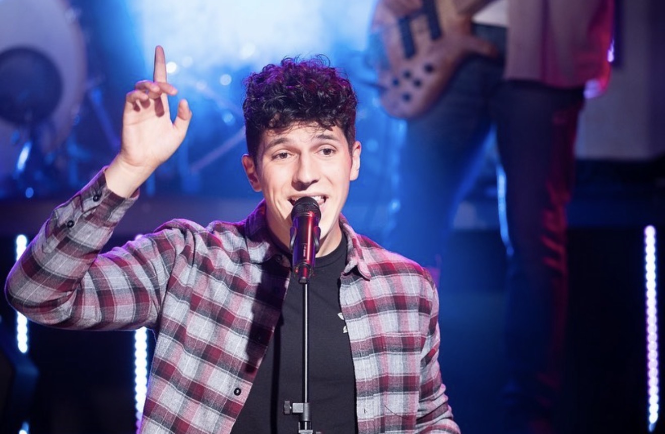 ILIJA performing at a microphone under blue and pink stage lights with his band