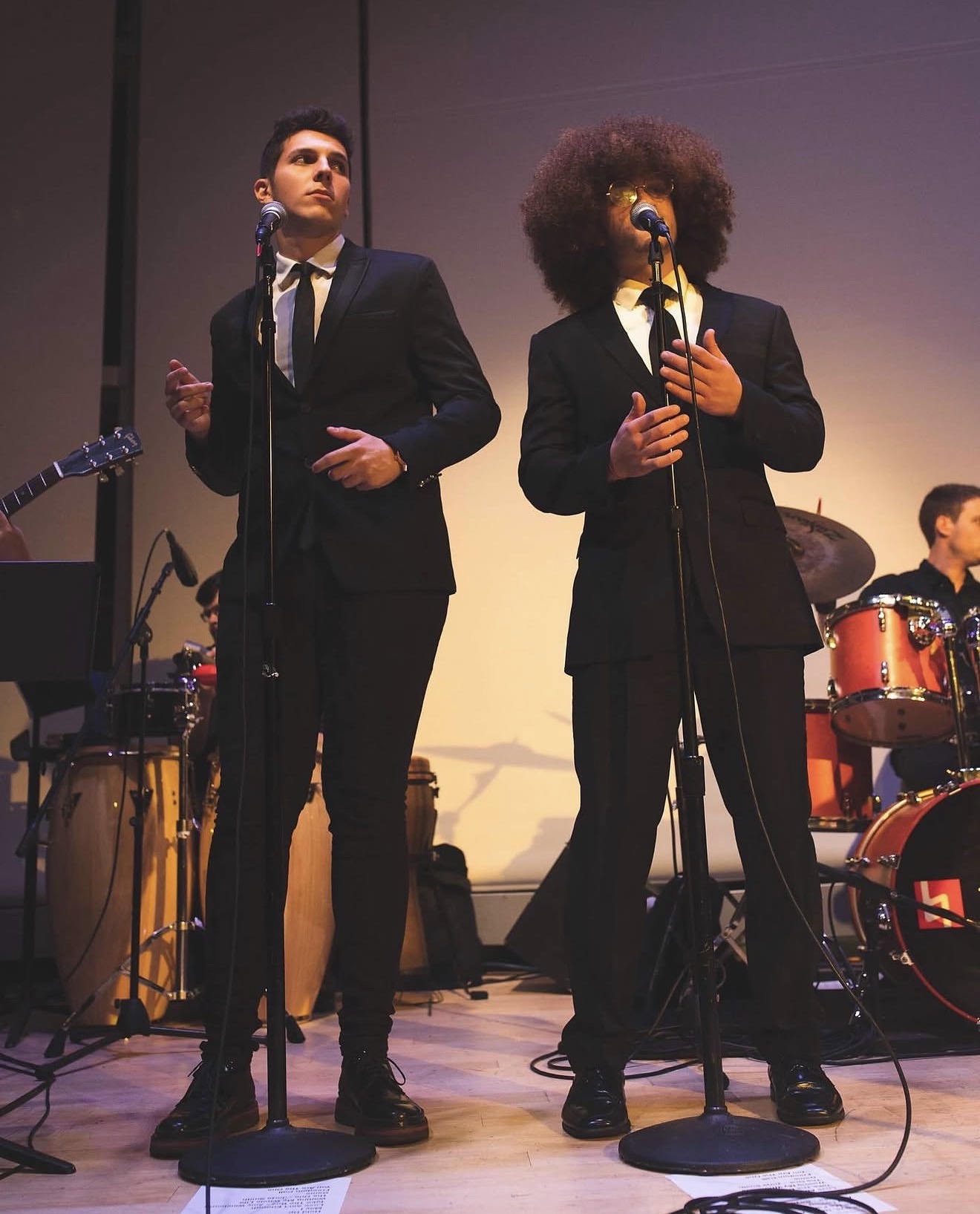 ILIJA in a black suit performing a duet at a concert hall microphone