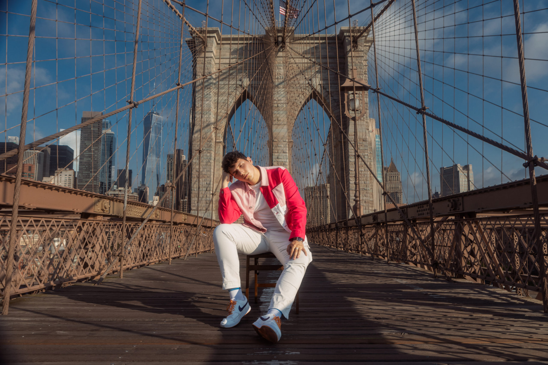 ILIJA leaning on his hand while seated mid-span on the Brooklyn Bridge