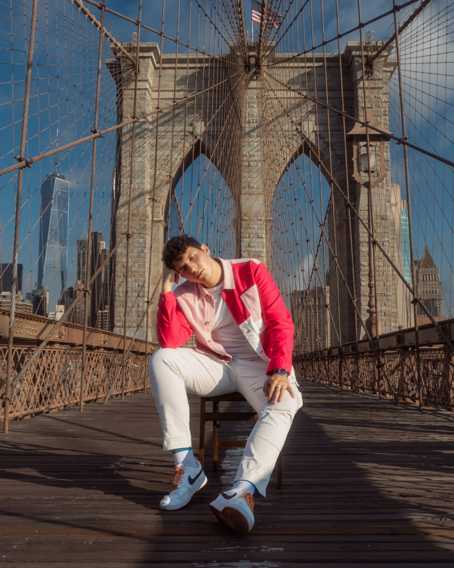 ILIJA resting his head on his hand while seated on a chair beneath the Brooklyn Bridge arches
